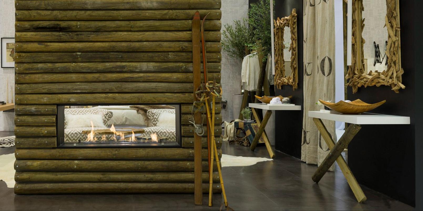 Projeto de design de interiores de quarto em refúgio da montanha onde os materiais naturais e tons neutros dominam o espaço. Detalhe de quarto com lareira revestida a troncos de madeira e apontamentos decorativos na zona de casa de banho.